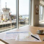 Premium editorial image of a Sydney apartment development site seen through a boardroom window, with feasibility papers on the table, representing NSW housing supply and foreign investment policy.