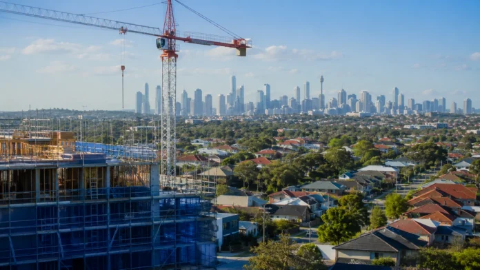 Construction crane and unfinished apartment building overlooking Sydney homes and skyline, illustrating the housing supply gap as migration outpaces new home building.