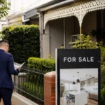 Property professional reviewing documents beside a for-sale sign outside an established Australian home, illustrating debate over housing tax changes and supply