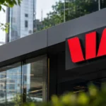 Westpac-style bank branch signage on a modern glass building, framed by greenery in an Australian city setting. 