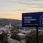 Regional Australian town at dusk with a new homes billboard overlooking suburban streets and hills, reflecting investor interest in regional housing supply.