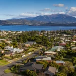 A wide view of Tasmanian suburban housing beside water and mountains, reflecting the infrastructure and supply challenge behind the 4,000-home housing deal.