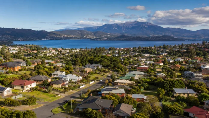 A wide view of Tasmanian suburban housing beside water and mountains, reflecting the infrastructure and supply challenge behind the 4,000-home housing deal.