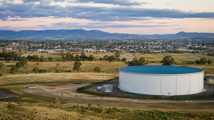 Aerial view of a large water storage tank beside new housing estates and open land near Toowoomba, showing infrastructure supporting regional housing supply.