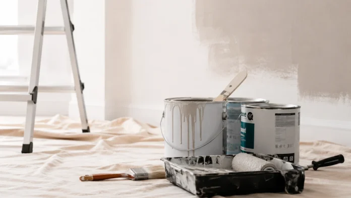 Paint cans, roller tray and brushes on a drop sheet inside a freshly painted Australian home interior.