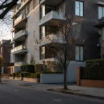 Quiet early-morning Australian residential street with low-rise apartments and brick townhouses, reflecting weaker housing confidence and a potential price correction.