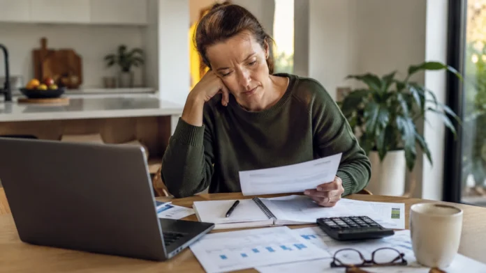 A woman reviews household bills and budget paperwork at a kitchen table, reflecting the financial pressure of rising living costs in Australia.