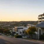 Early-morning regional Australian streetscape with modest homes, a low-rise apartment building and limited street parking, reflecting housing supply pressure and resilient regional property markets.